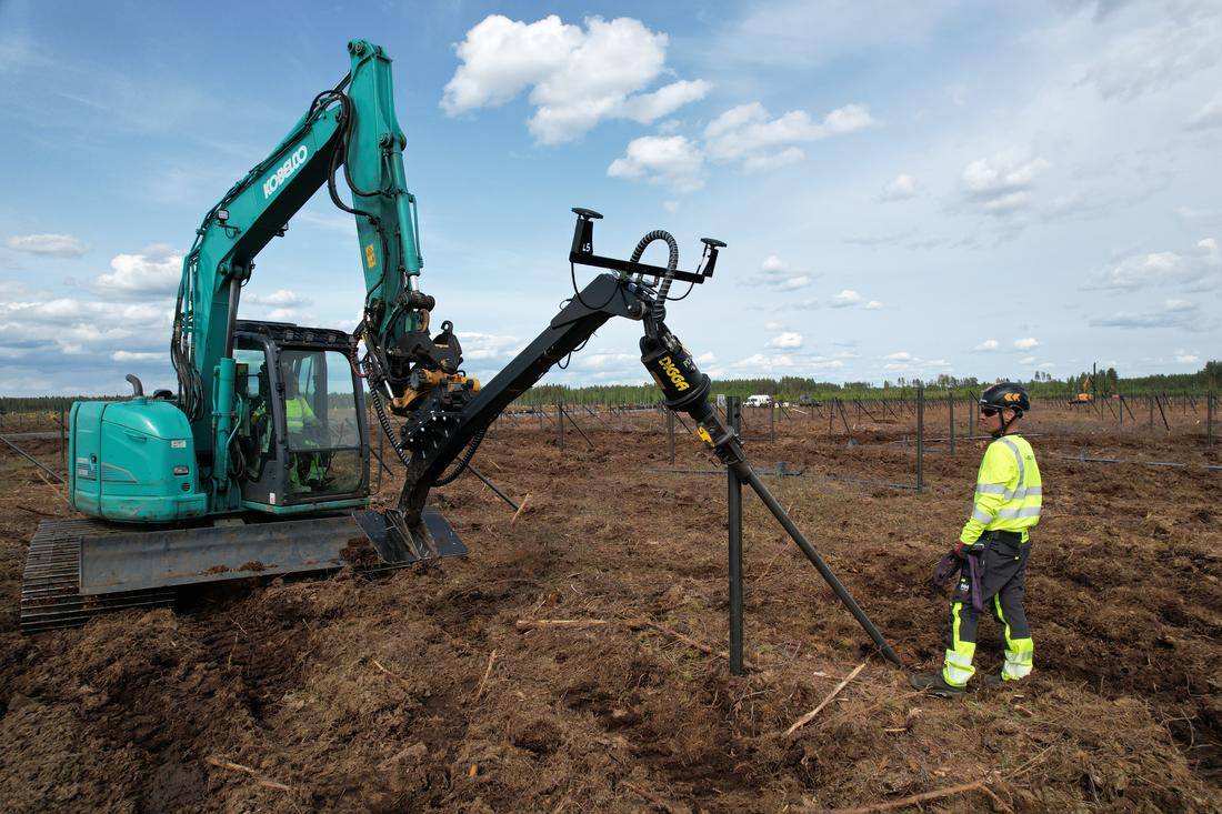 GPS-guided installation crew driving helical piles on solar park site